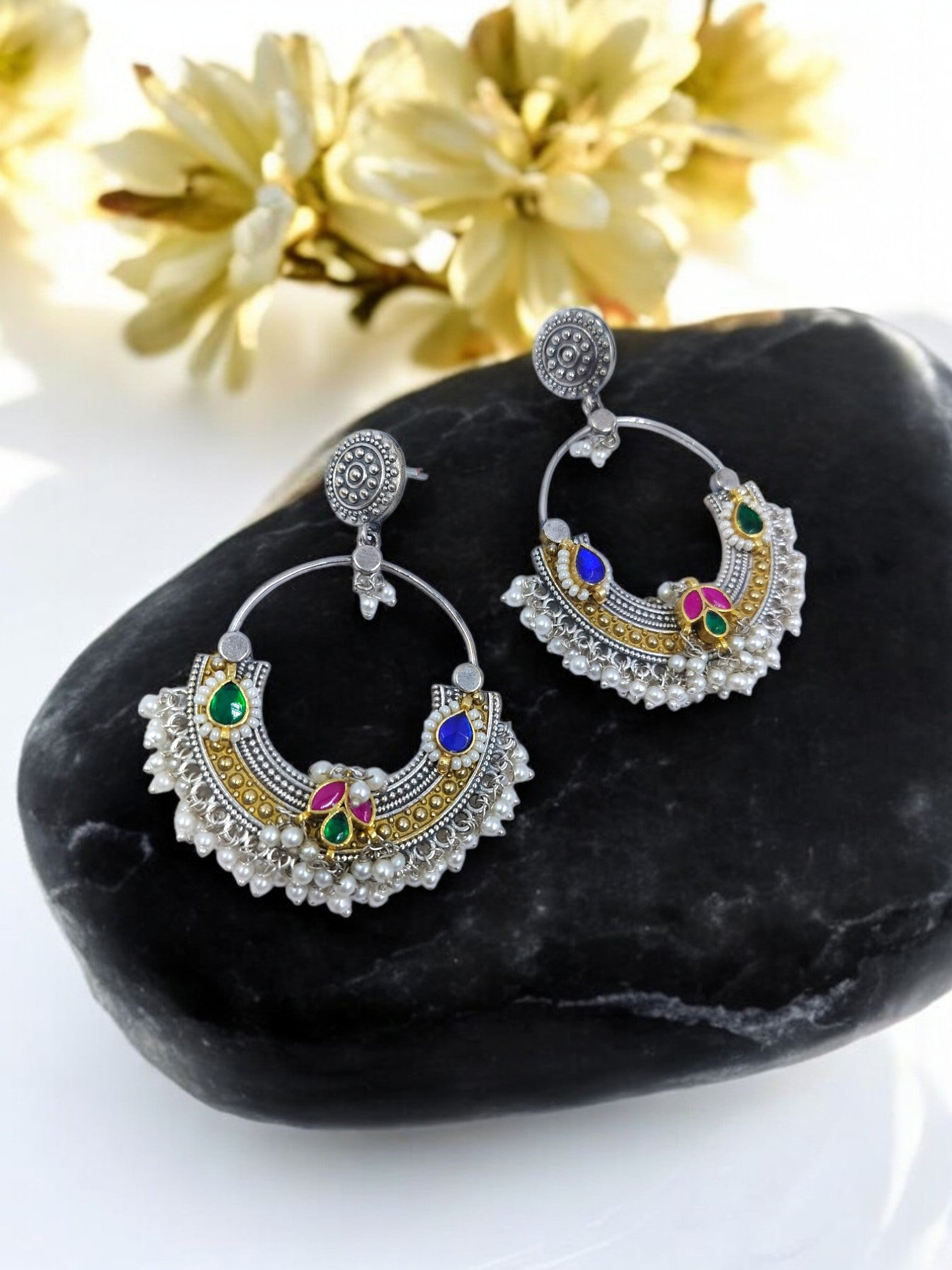 Antique Bareilly jhumka earrings with silver filigree, adorned with green, pink, and blue gemstones on a rock.