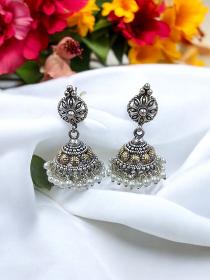 Antique oxidized silver jhumka earrings with floral carvings, golden detailing, and pearl drops – perfect for ethnic and festive wear.