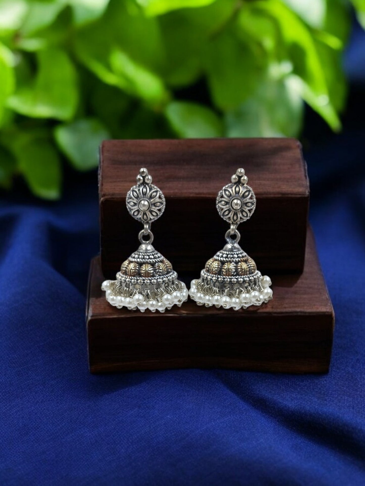 Antique Nayantara Jhumkis with floral design and golden accents, displayed on a wooden jewelry box.