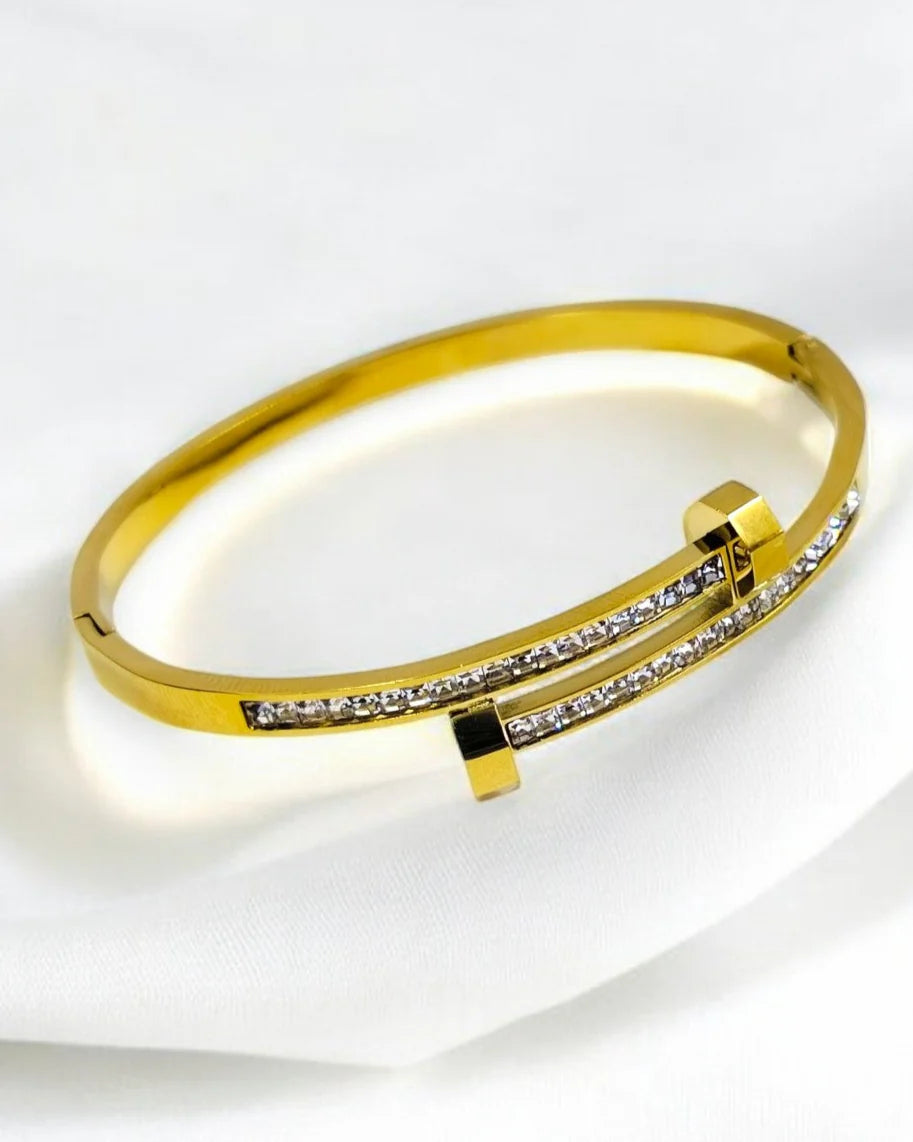 A gold-colored bangle bracelet with cubic zirconia stone embellishments.