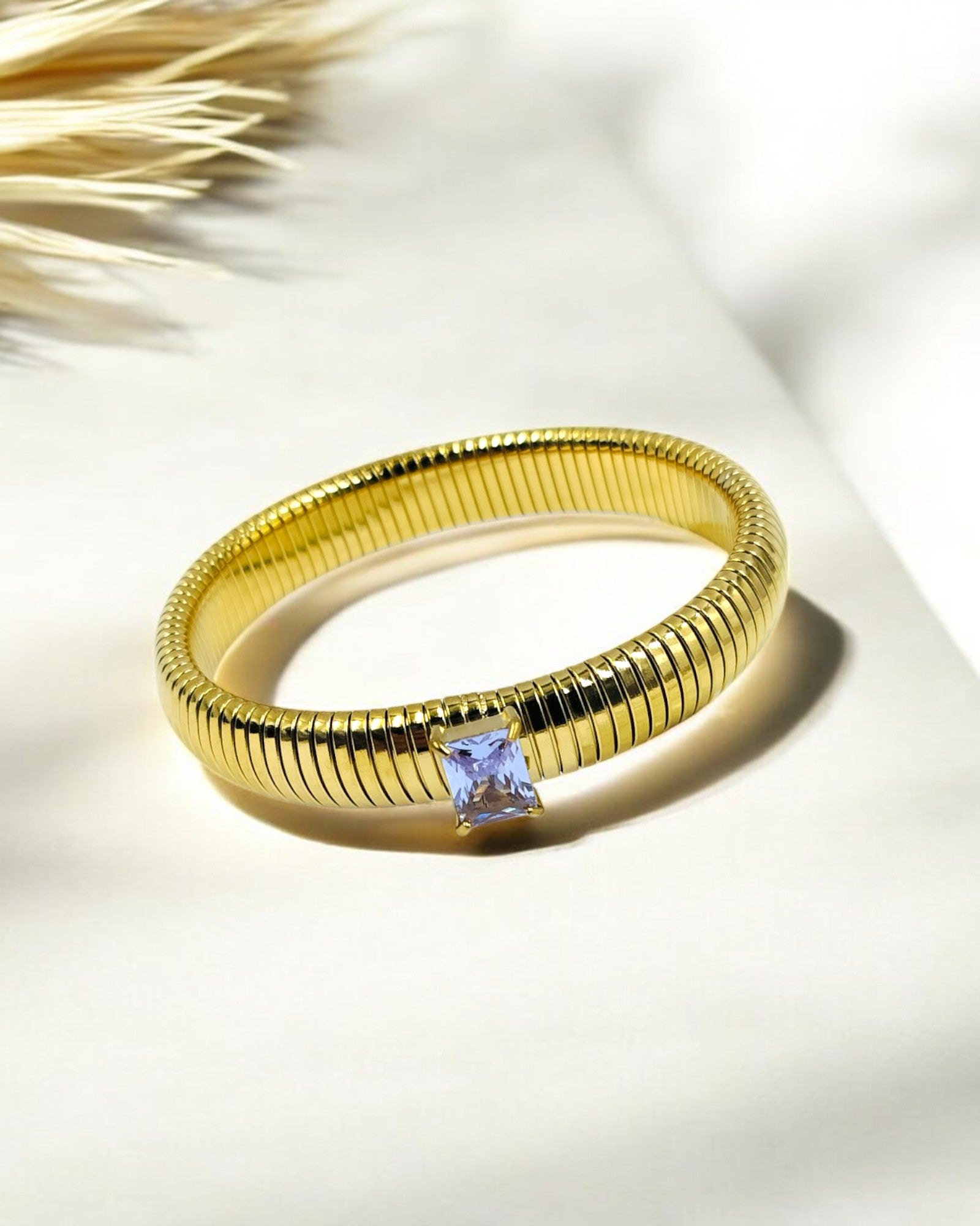 A gold-colored stretchable snake coil elastic bangle bracelet with a single clear zirconia stone on it, displayed against a light background.