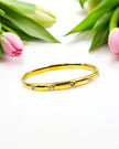 A gold-colored bracelet with diamond-like studs, displayed alongside pink tulips.