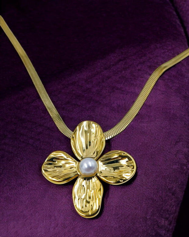 A gold floral pendant necklace with a pearl center on a snake chain against a purple background.