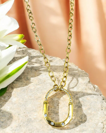 A gold-colored chain necklace with a starfish pendant and pearl details, displayed on a stone surface with a flower in the background.