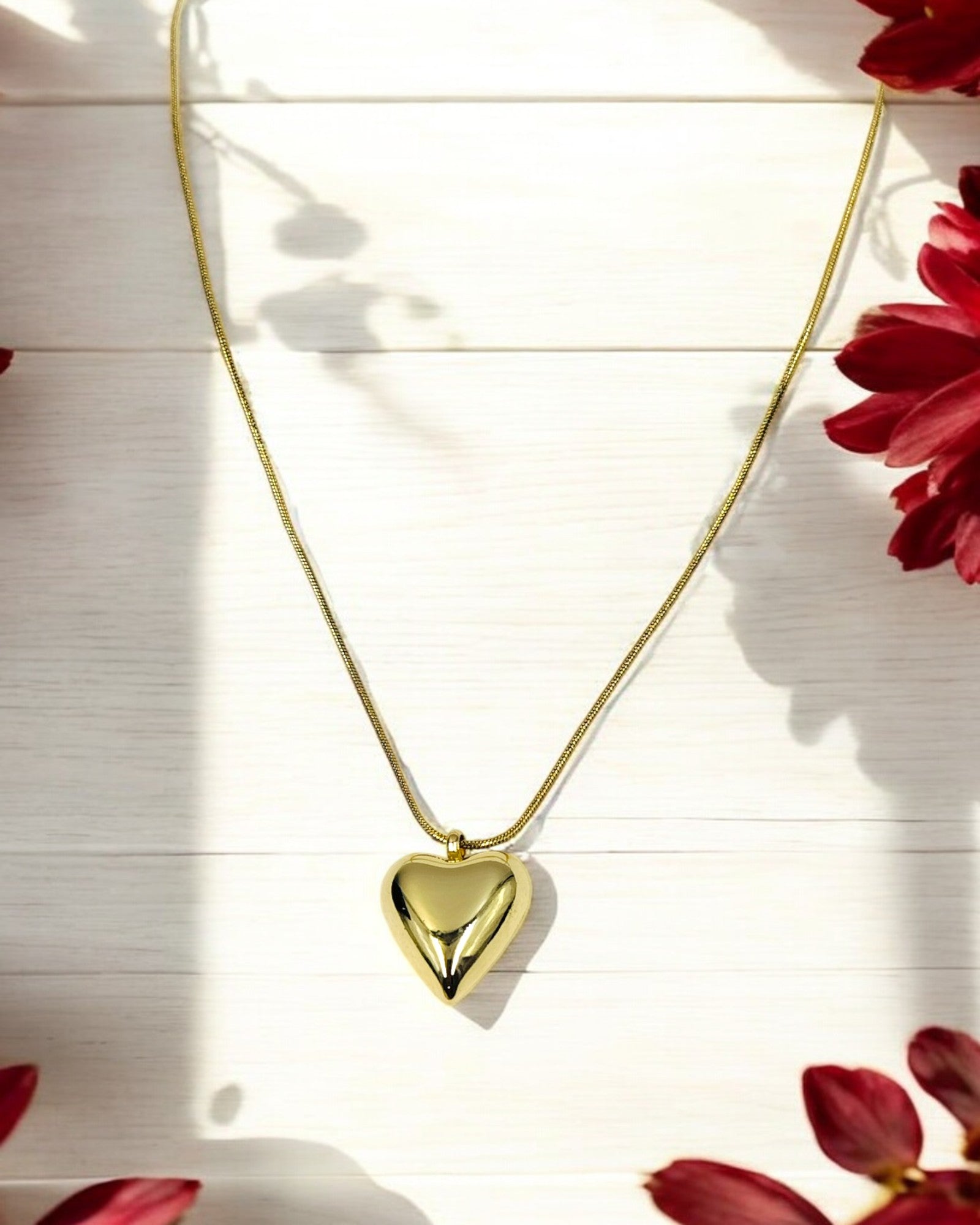A gold-colored heart pendant chain necklace laid out on a flat surface with a floral pattern in the background.