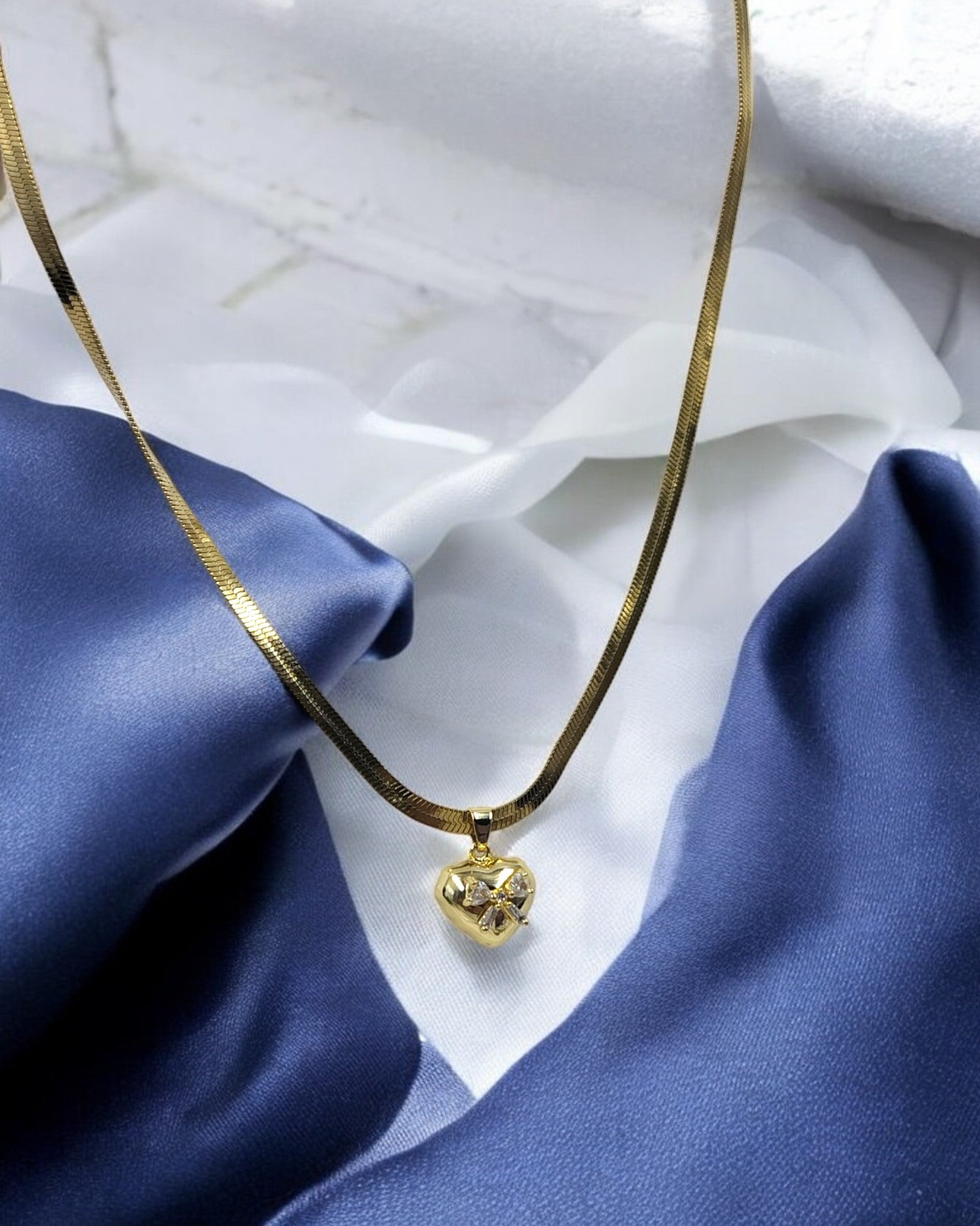 Elegant gold plated necklace with heart shaped crystal pendant on blue satin fabric – Glampouch jewelry