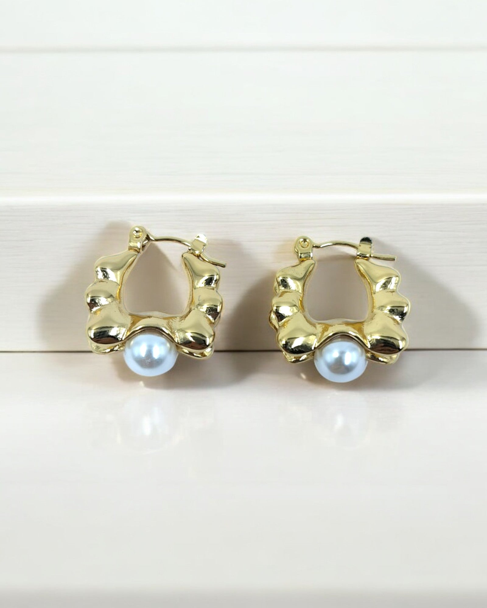 A pair of gold-colored faux pearl hoop earrings placed against a light wooden background.