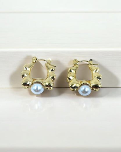 A pair of gold-colored faux pearl hoop earrings placed against a light wooden background.