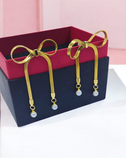 Gold bow-shaped earrings with long dangling strands and pearl drops for a stylish and feminine statement look.