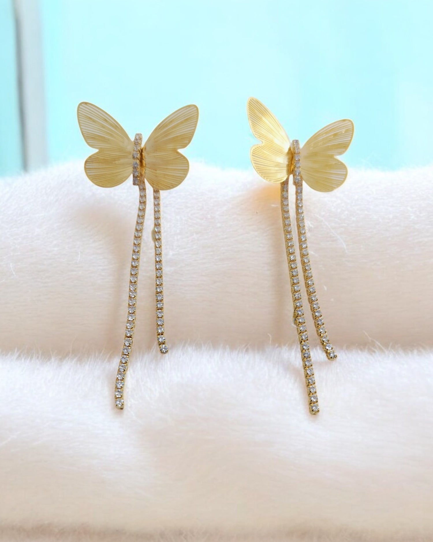 A pair of gold-plated butterfly earrings with diamond rhinestone tassels displayed on a white surface.