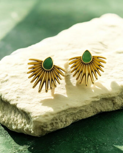 Gold fan-shaped earrings with green gemstone center, modern statement jewellery displayed on stone with natural light