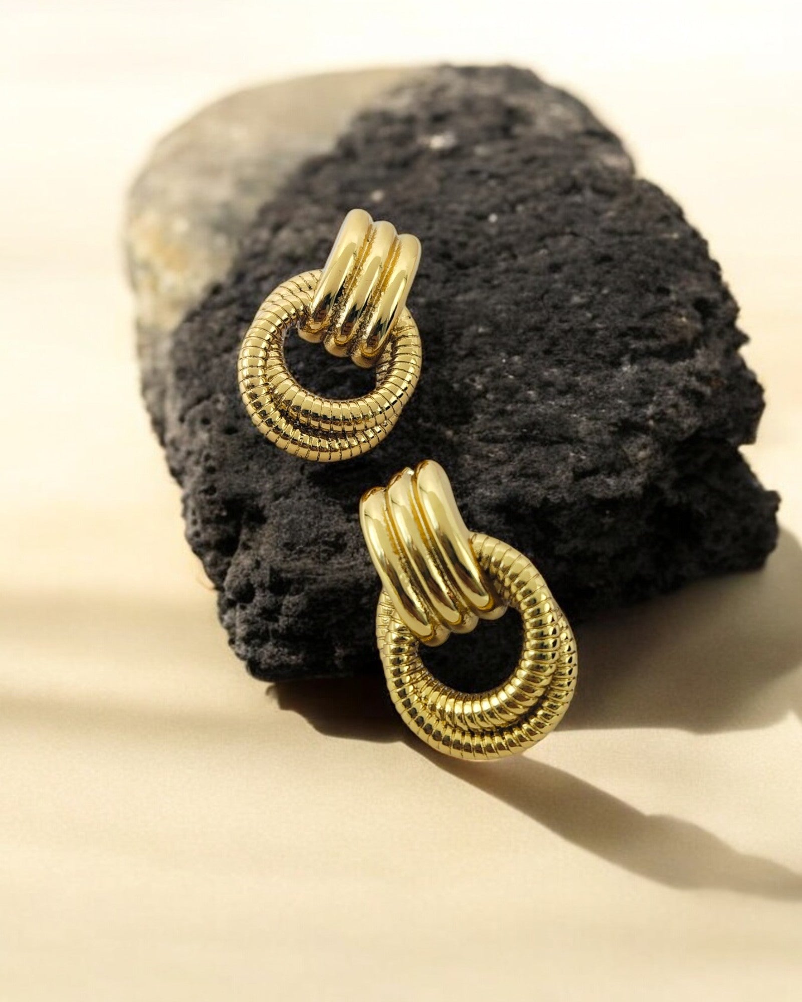 Textured gold loop earrings with layered circular design placed on a black stone, elegant statement jewellery piece