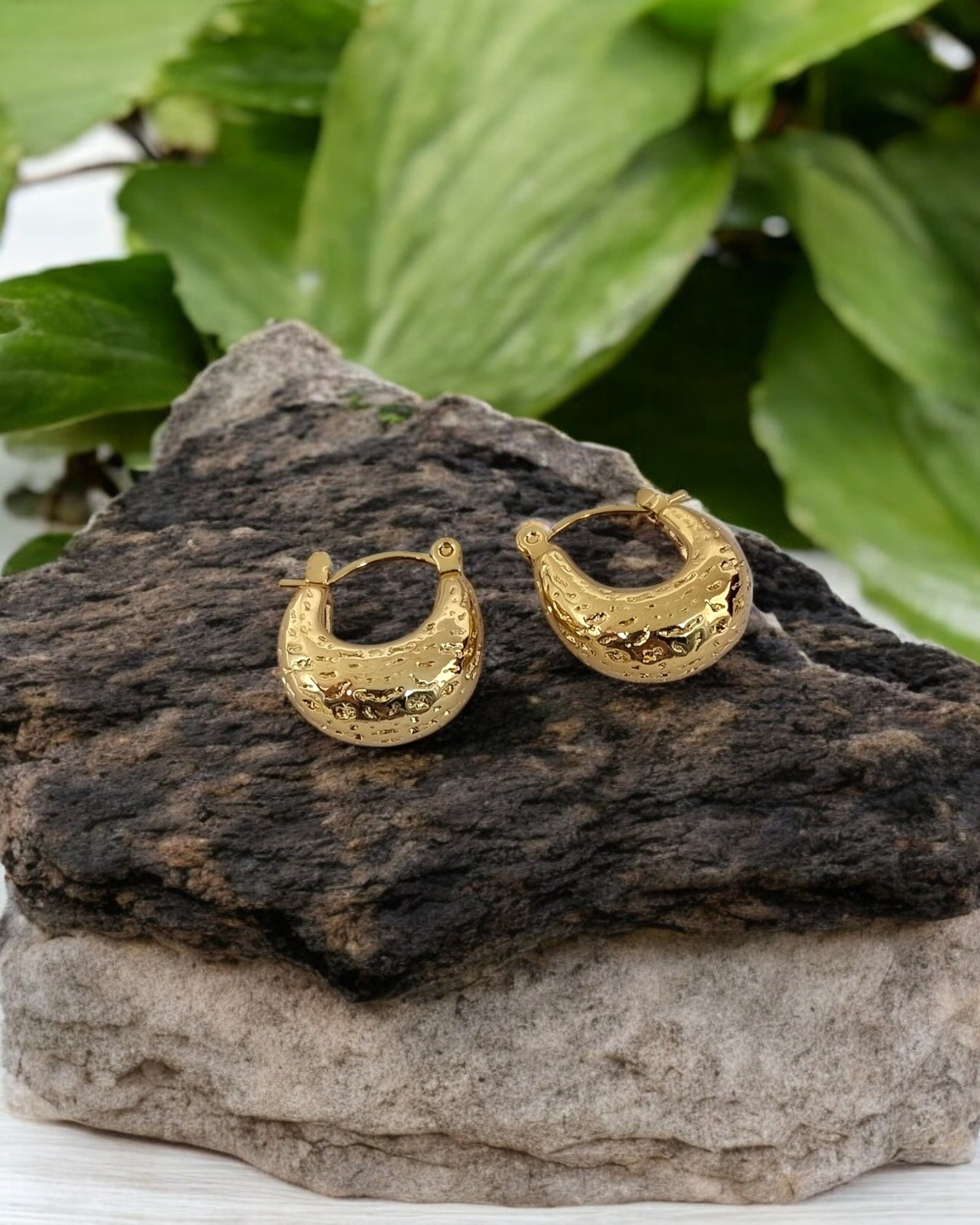 Textured gold hoop earrings placed on natural stone with green leaves, stylish boho chic jewellery for everyday wear