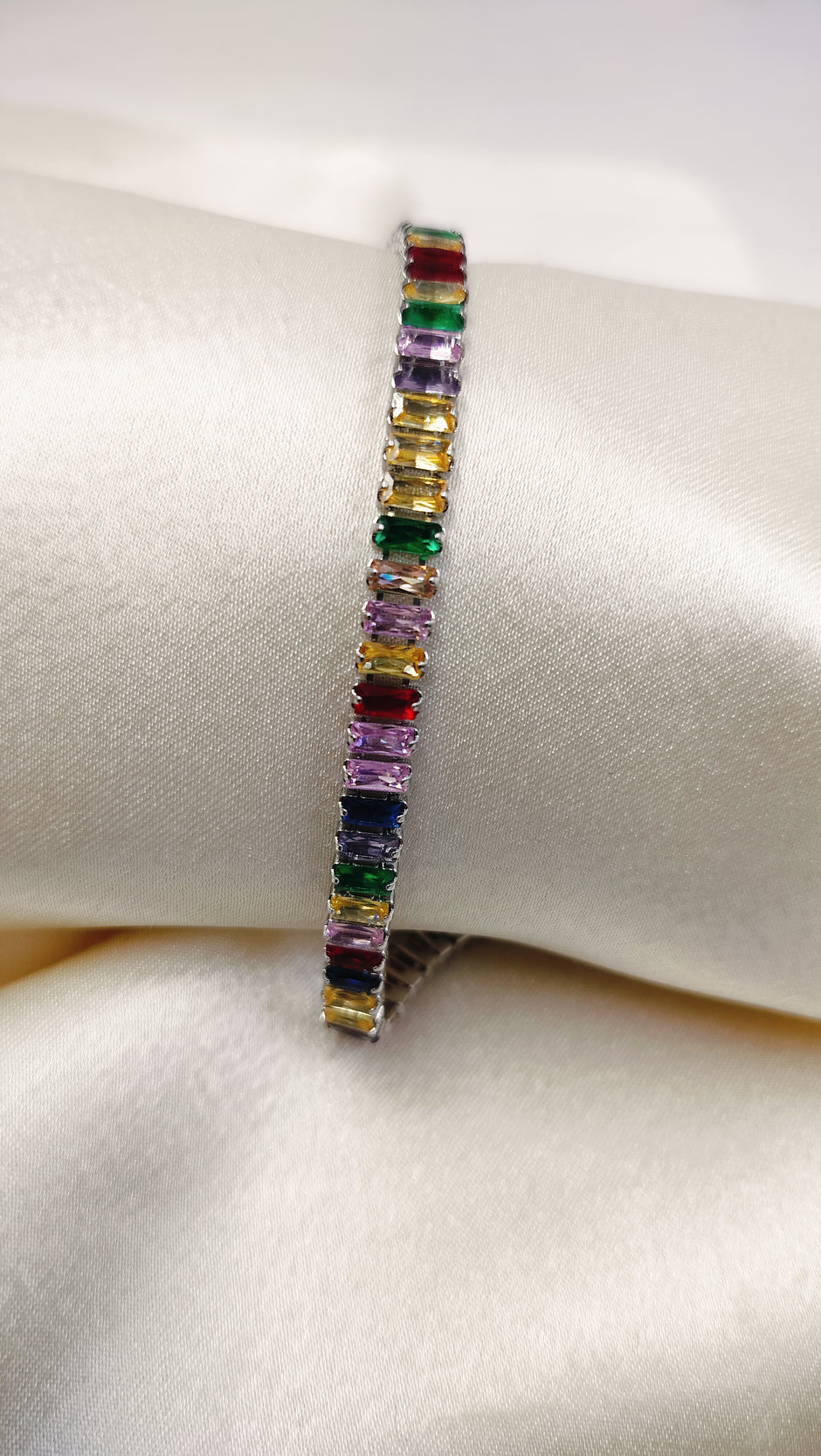 A white gold plated tennis bracelet featuring multi-colored cubic zirconia stones, displayed on a white surface.