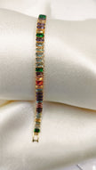 Gold tennis bracelet with multicolored baguette-cut cubic zirconia stones on a satin pillow.