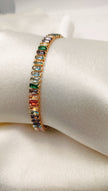 A gold-plated tennis bracelet featuring multi-colored cubic zirconia stones displayed on a white surface.
