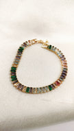Elegant gold-toned bracelet featuring a vibrant row of multicolored rectangular gemstones, displayed on a textured white background.