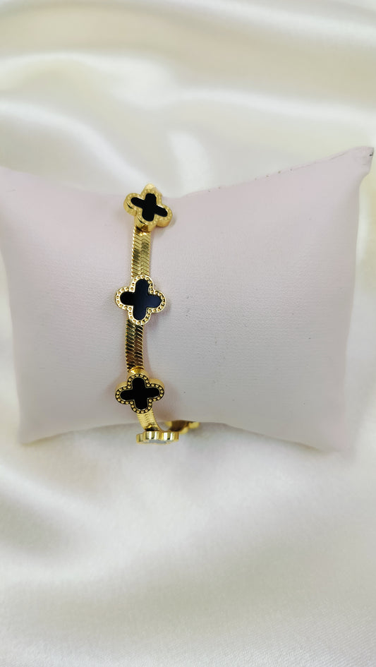 A gold-plated bracelet with a herringbone design displayed on a white cushion.