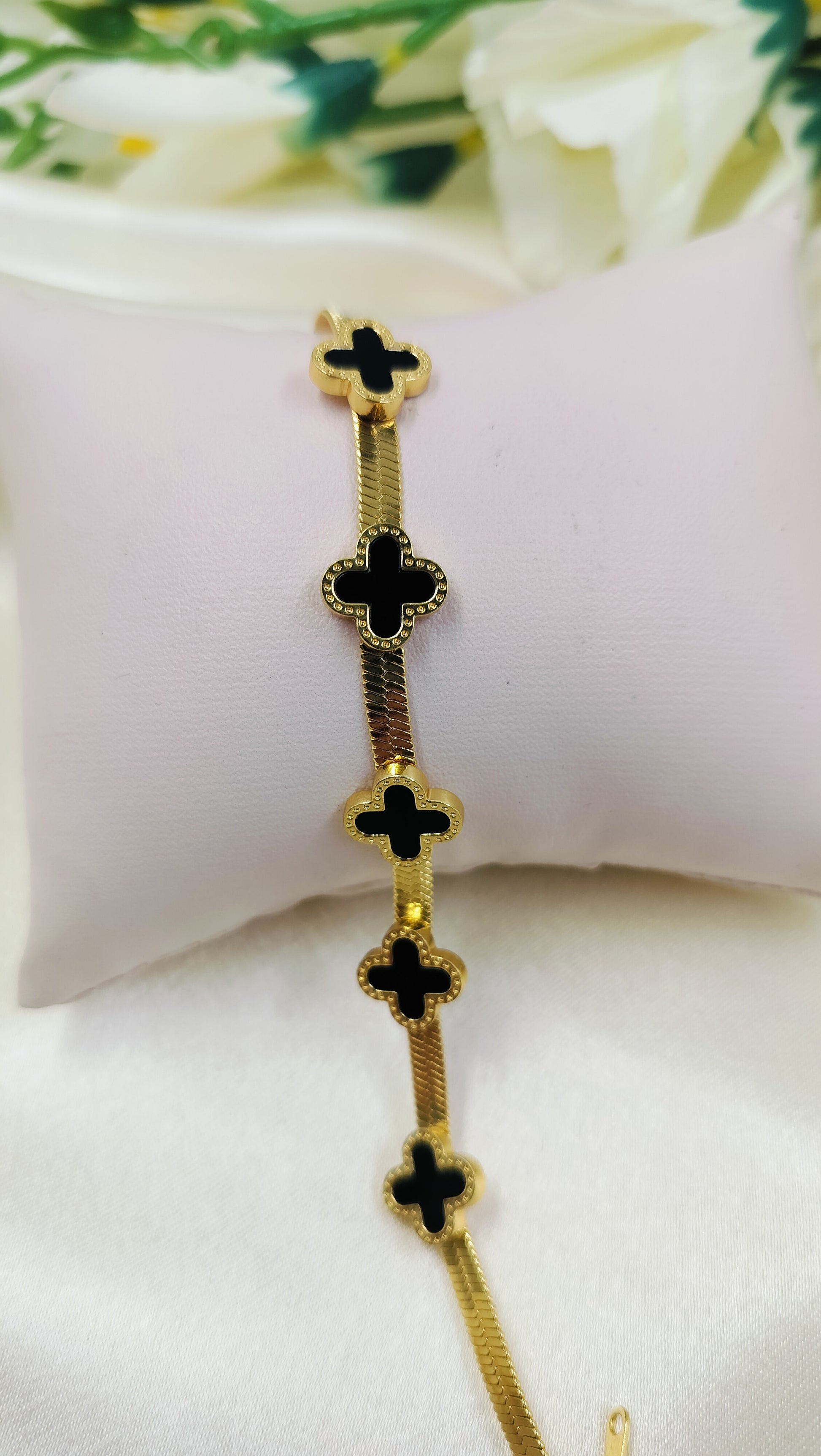 Gold snake chain bracelet with five black onyx clover motifs.