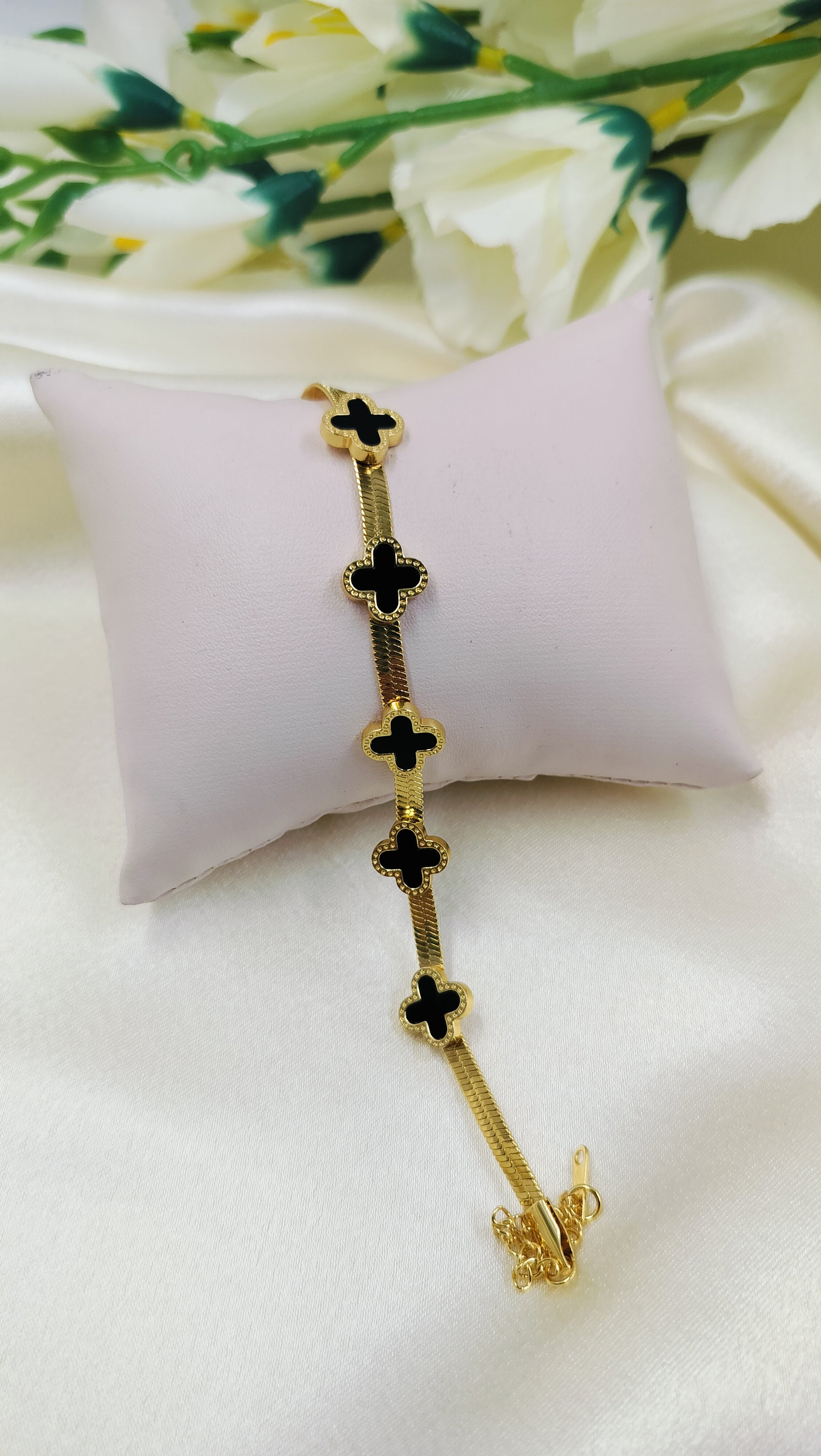 Gold snake chain bracelet with five black onyx clover motifs.