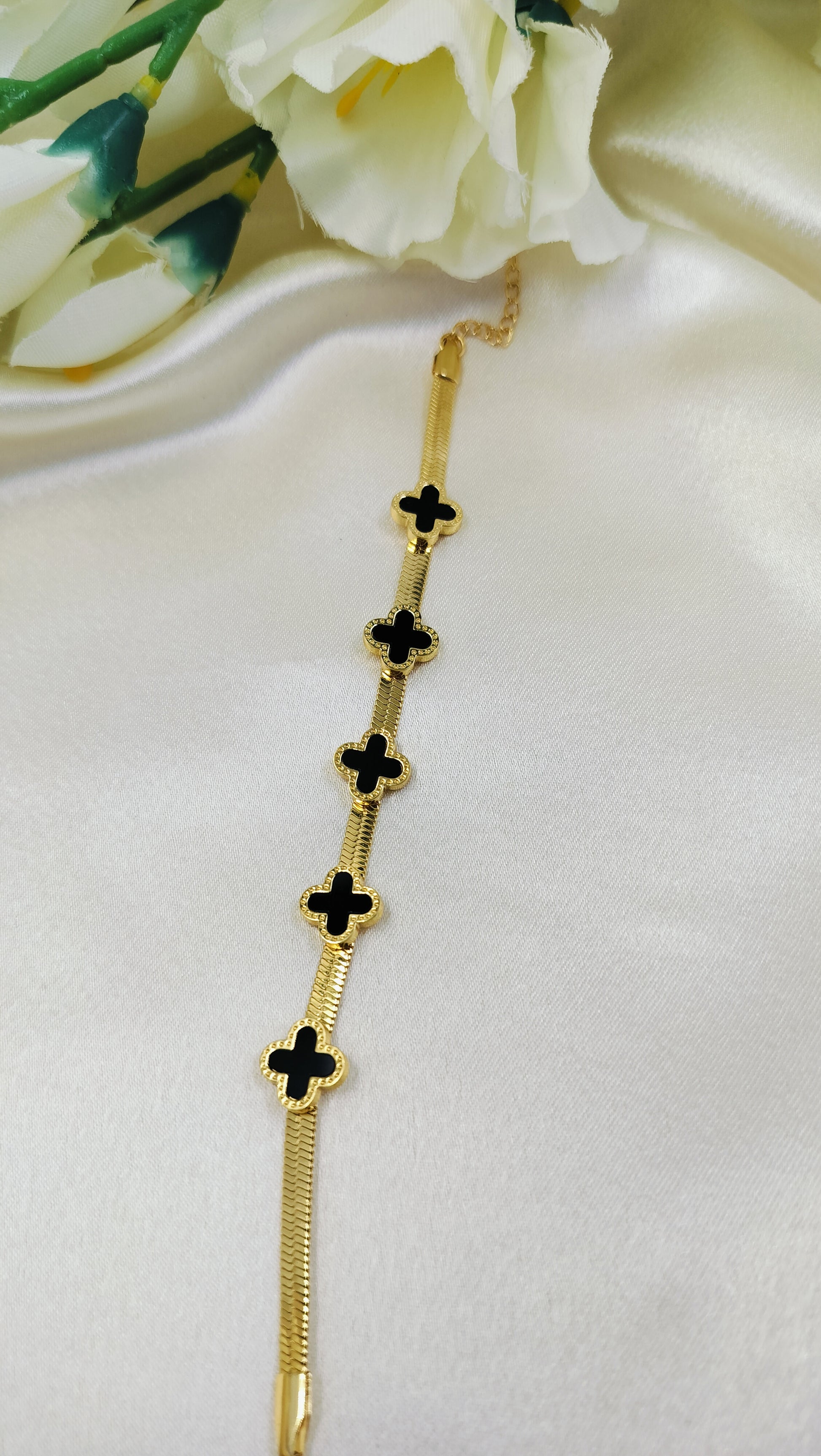 Gold snake chain bracelet with five black onyx clover motifs.