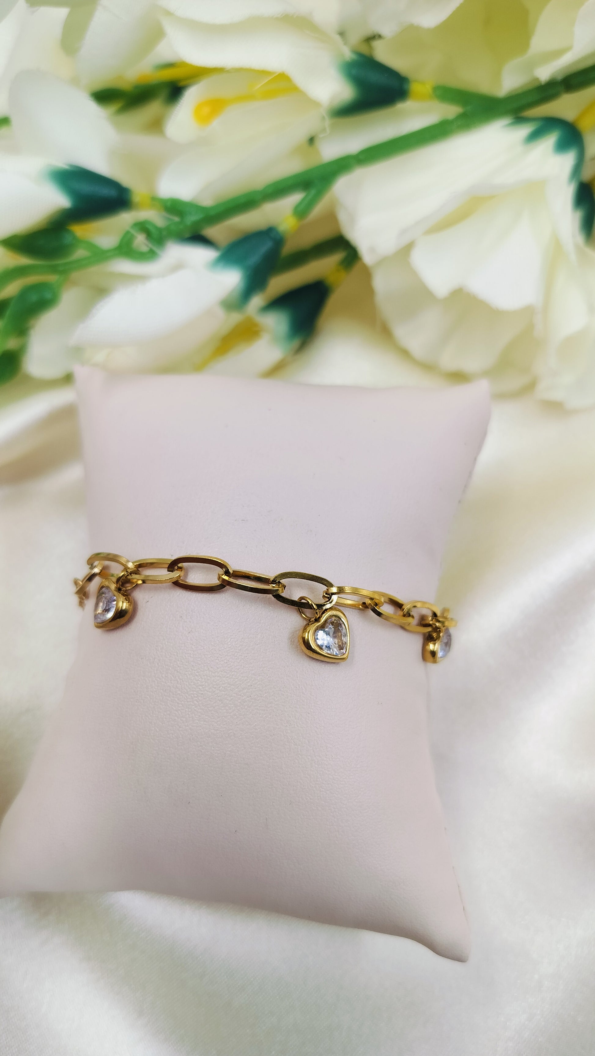 Gold chain link bracelet with three heart-shaped pendants and white stones on a pillow