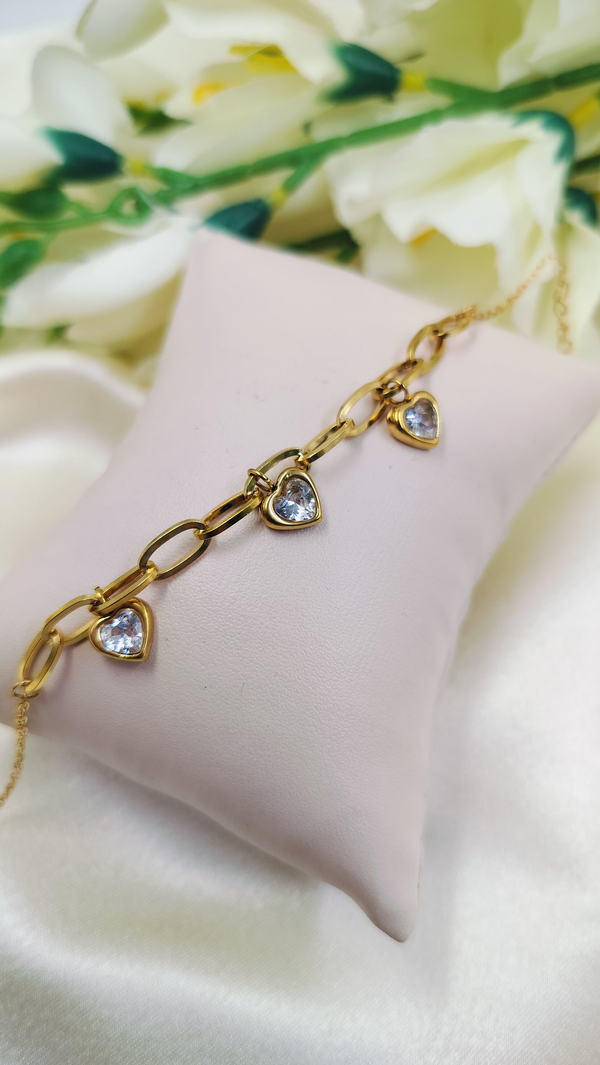 Gold chain link bracelet with three heart-shaped pendants and white stones.