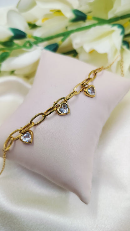 Gold chain link bracelet with three heart-shaped pendants and white stones.