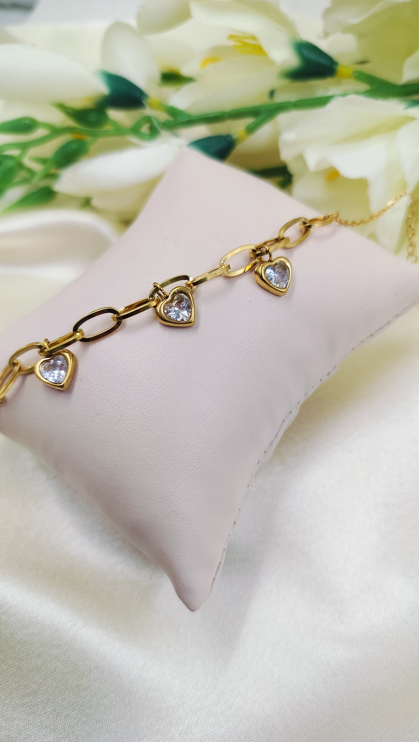 Gold chain link bracelet with three heart-shaped pendants and white stones on a pillow
