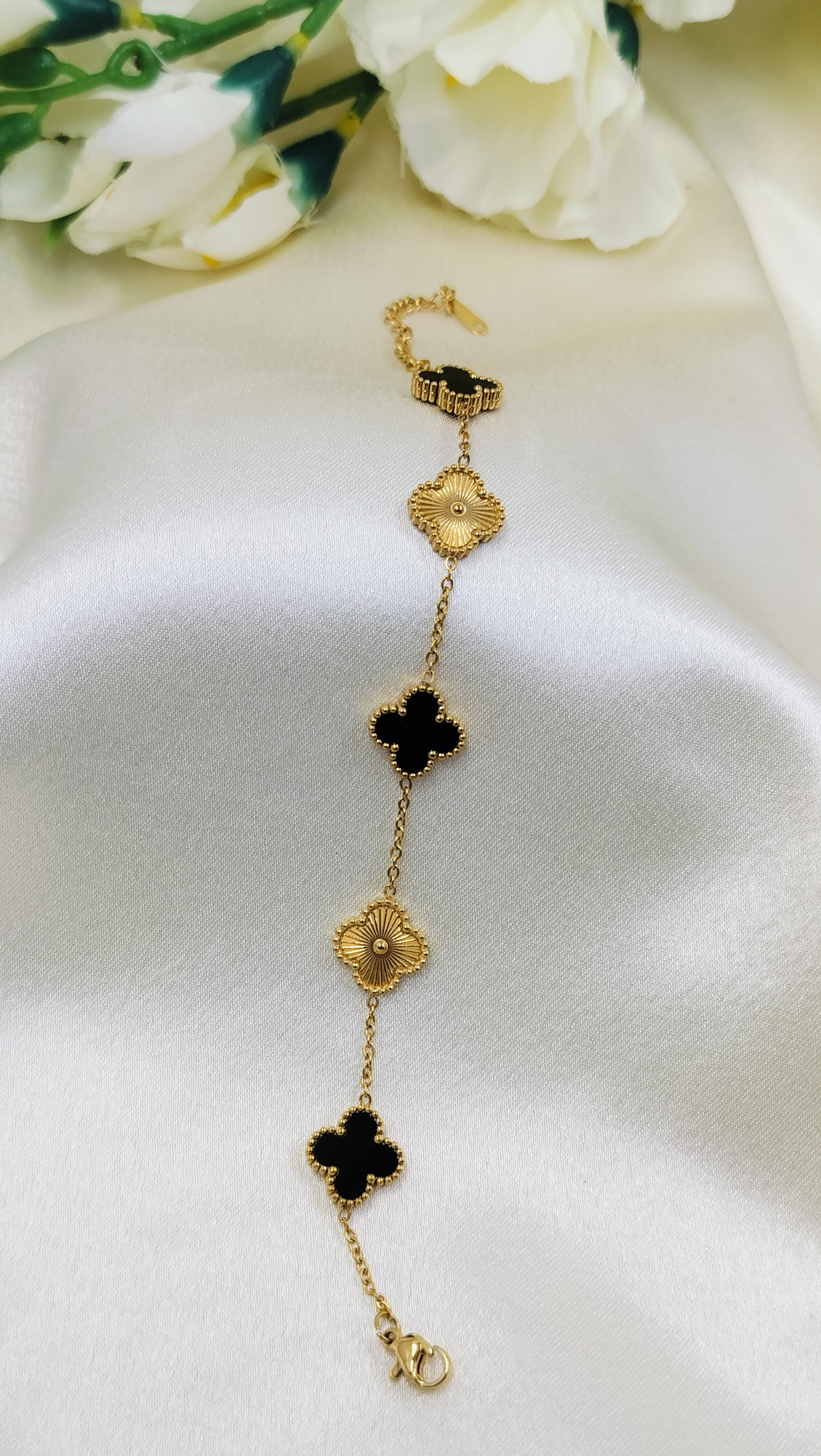 Gold chain bracelet with alternating black and gold clover charms.