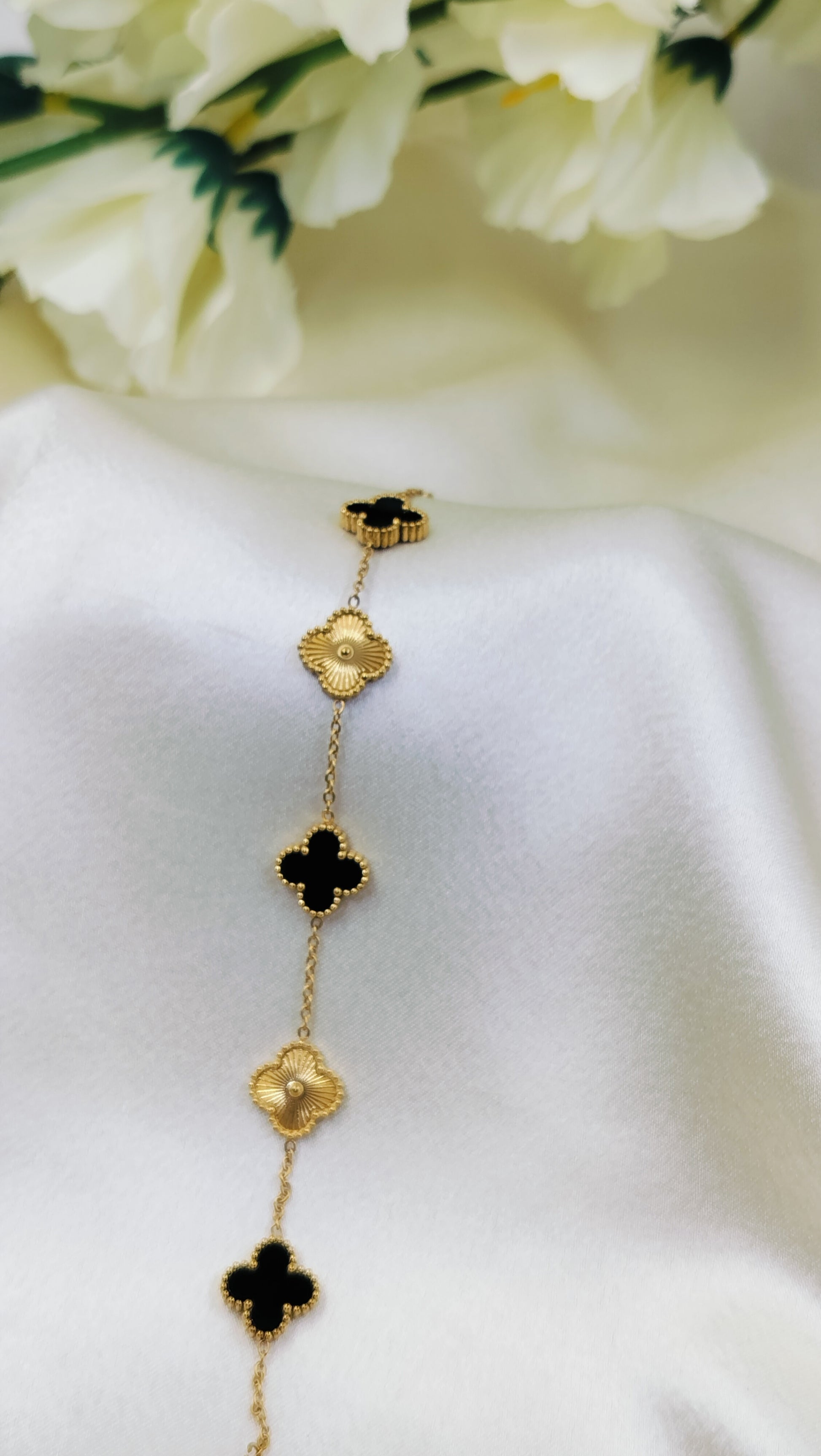 Gold chain necklace with black onyx clover motifs on white fabric and floral background.
