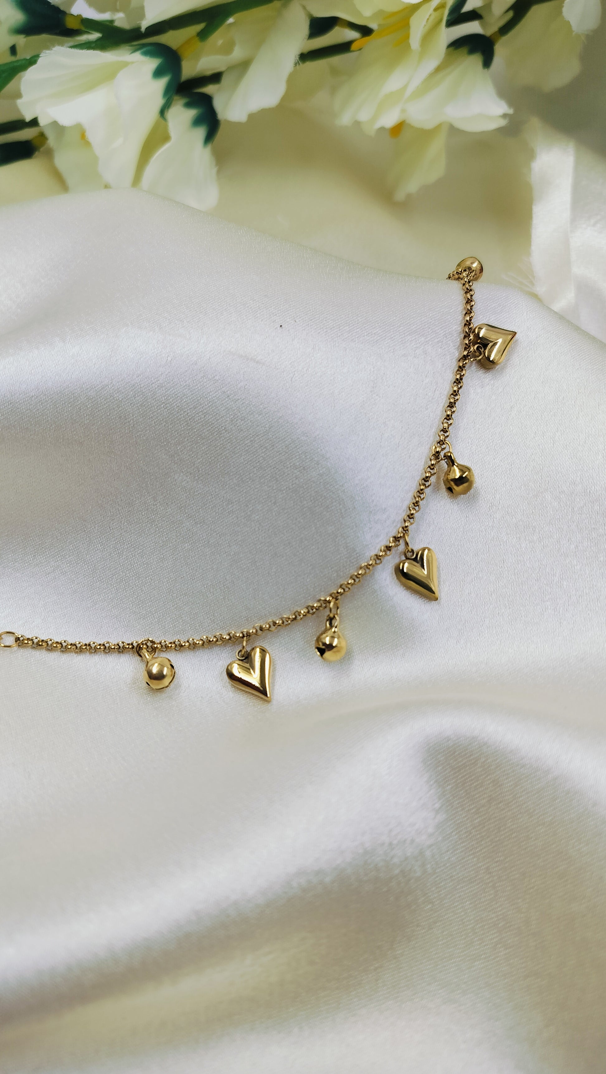 A gold-plated stainless steel bracelet with heart-shaped charms, displayed on a silky fabric.
