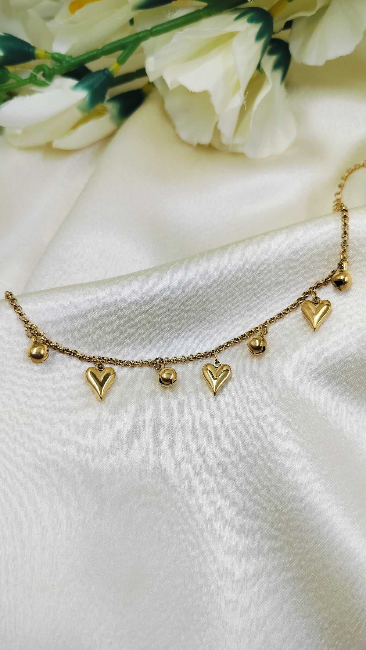 Elegant gold bracelet with dangling heart and bead charms, displayed on satin fabric – romantic handmade jewelry for women