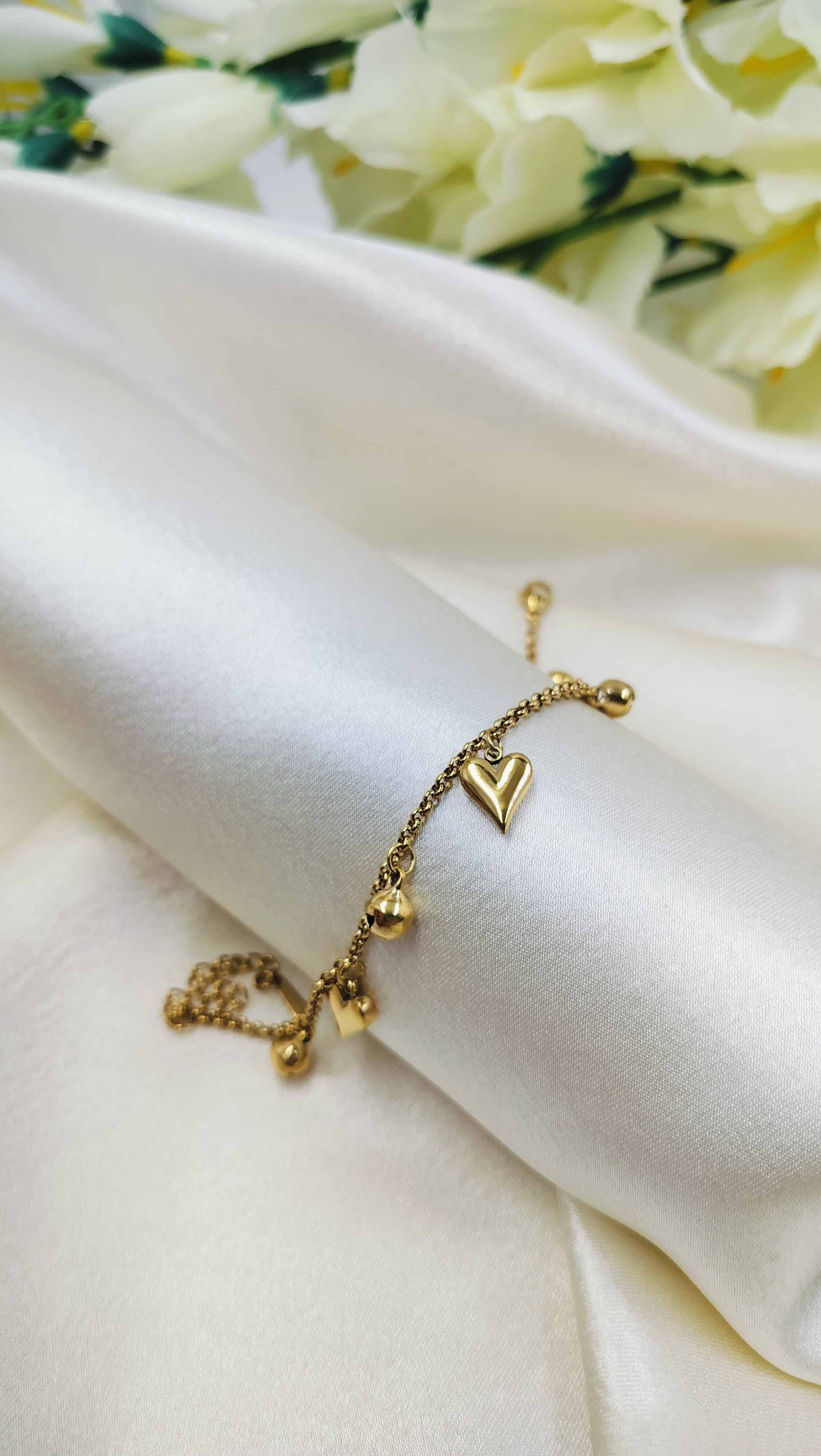 Minimal gold bracelet with heart charm and delicate beads, displayed on satin fabric – elegant handmade jewelry for women