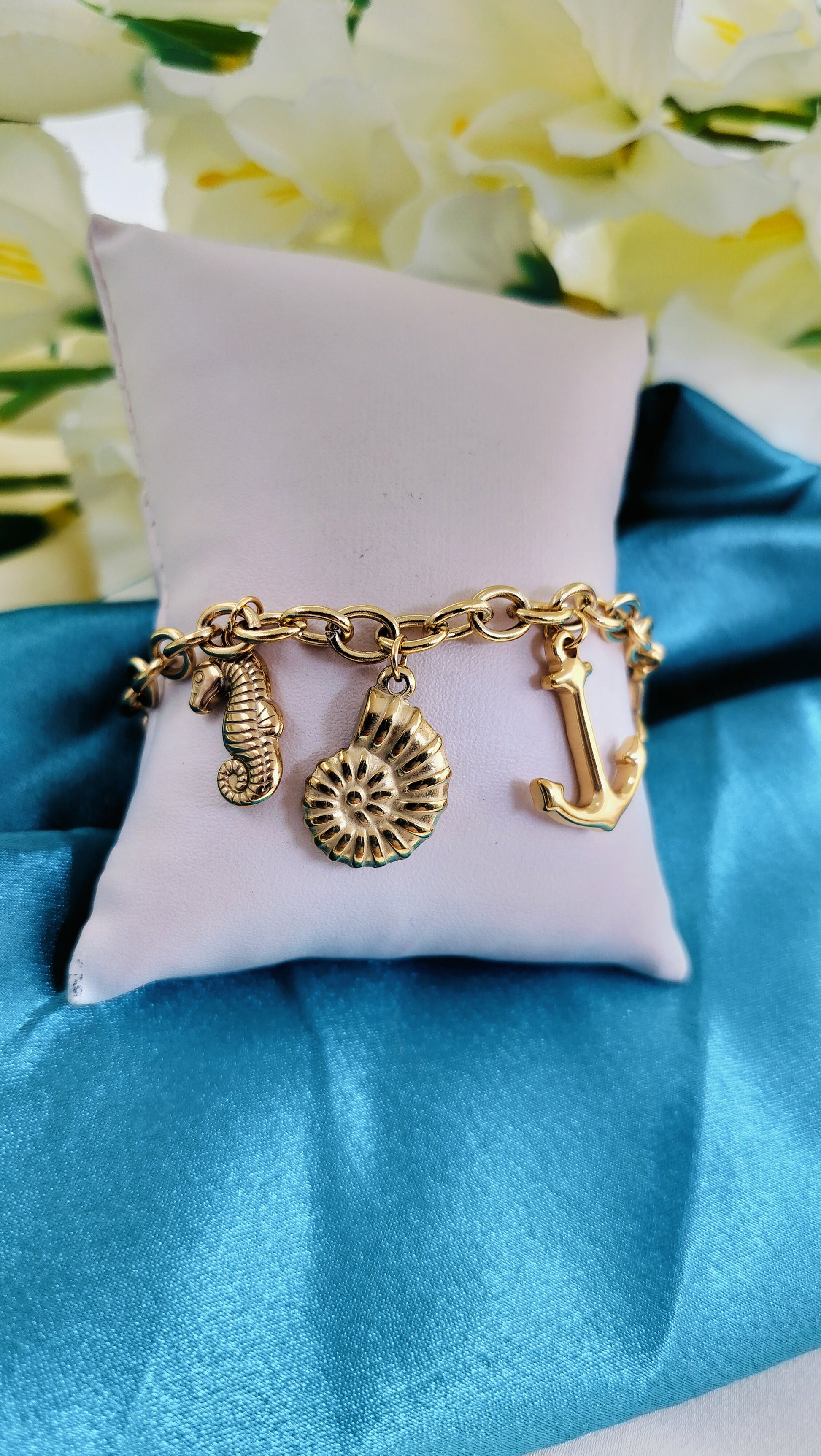 A gold-plated bracelet with ocean life charms, displayed on a white cushion with a blue fabric background.