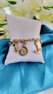 A gold-plated bracelet with ocean life charms, displayed on a white cushion with a blue fabric background.