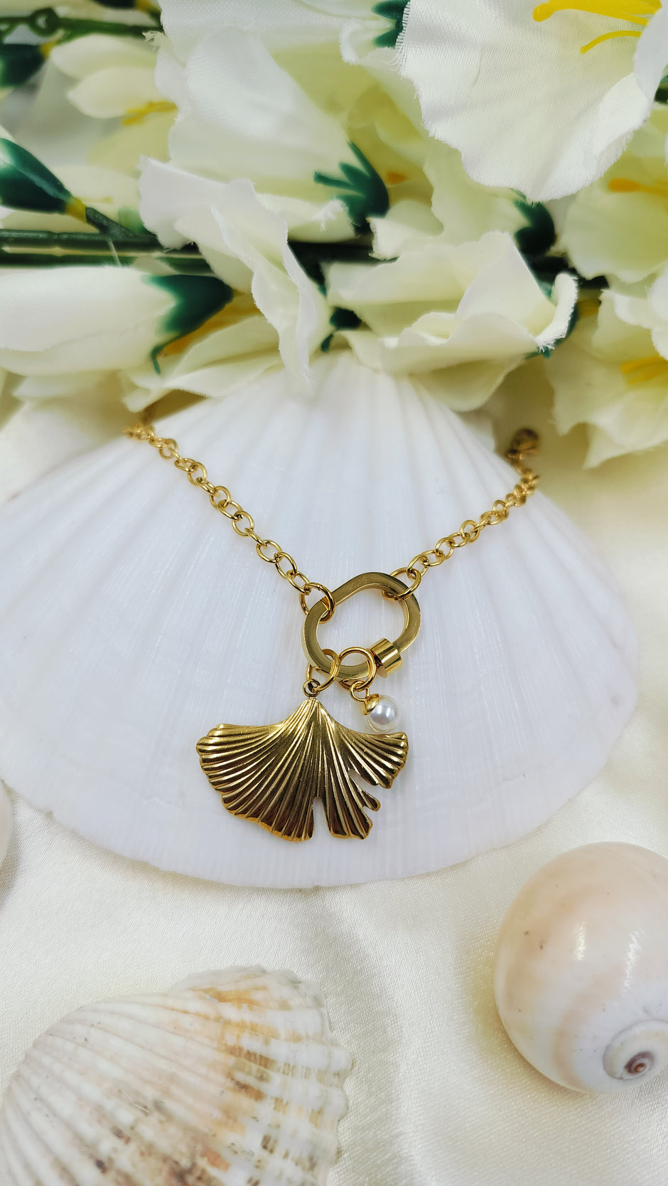 Elegant gold bracelet with ginkgo leaf charm and pearl detail, styled on seashell and flowers – perfect handmade jewelry for women