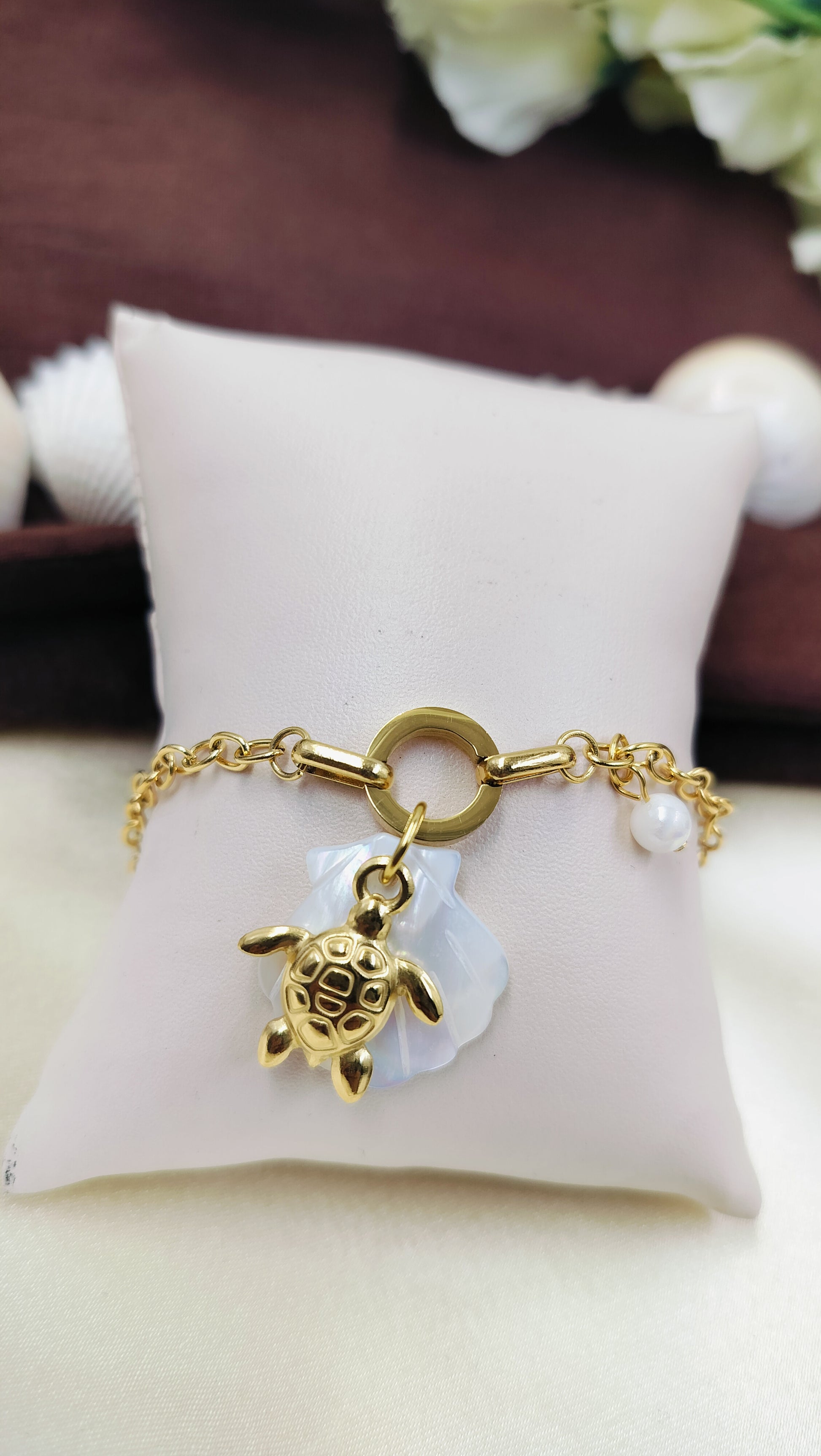 Gold bracelet with turtle charm, mother of pearl flower and pearl accent, displayed on cushion – stylish handmade jewelry for women