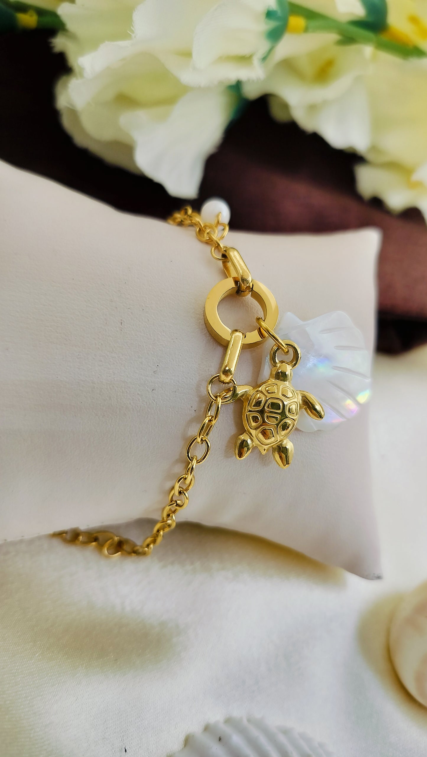 Gold bracelet with turtle charm, mother of pearl flower and pearl accent, displayed on cushion – stylish handmade jewelry for women
