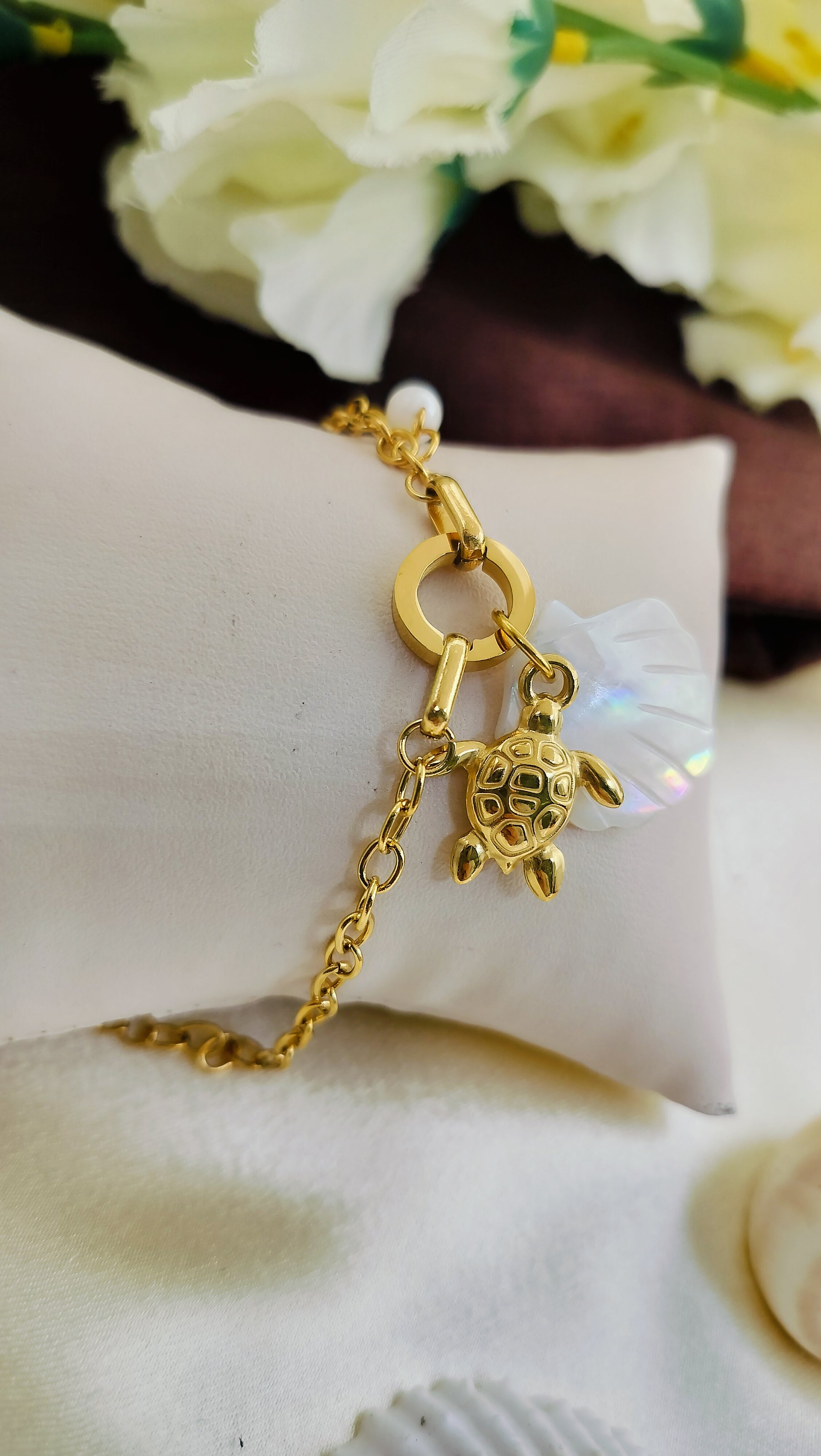 Gold bracelet with turtle charm, mother of pearl flower and pearl accent, displayed on cushion – stylish handmade jewelry for women