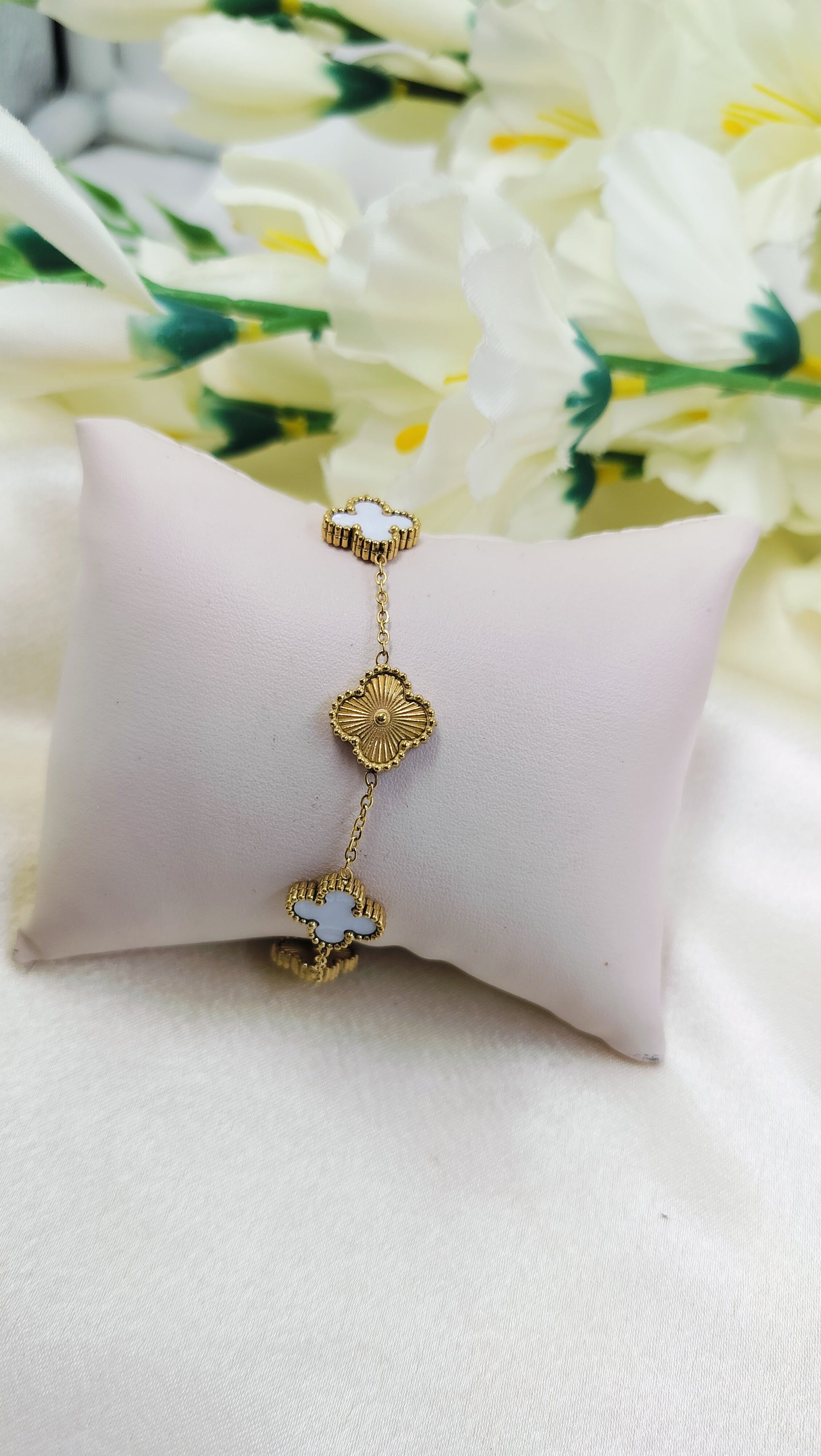 Elegant gold bracelet with alternating floral and white clover charms, displayed on cushion – luxury designer jewelry for women