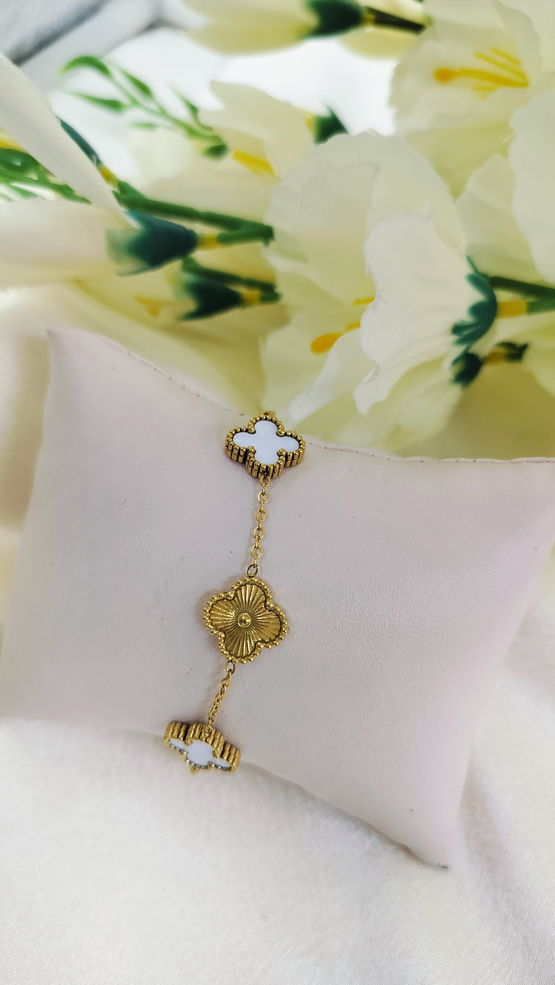 Gold bracelet with white clover and floral charm design, displayed on cushion with flowers – stylish luxury jewelry for women