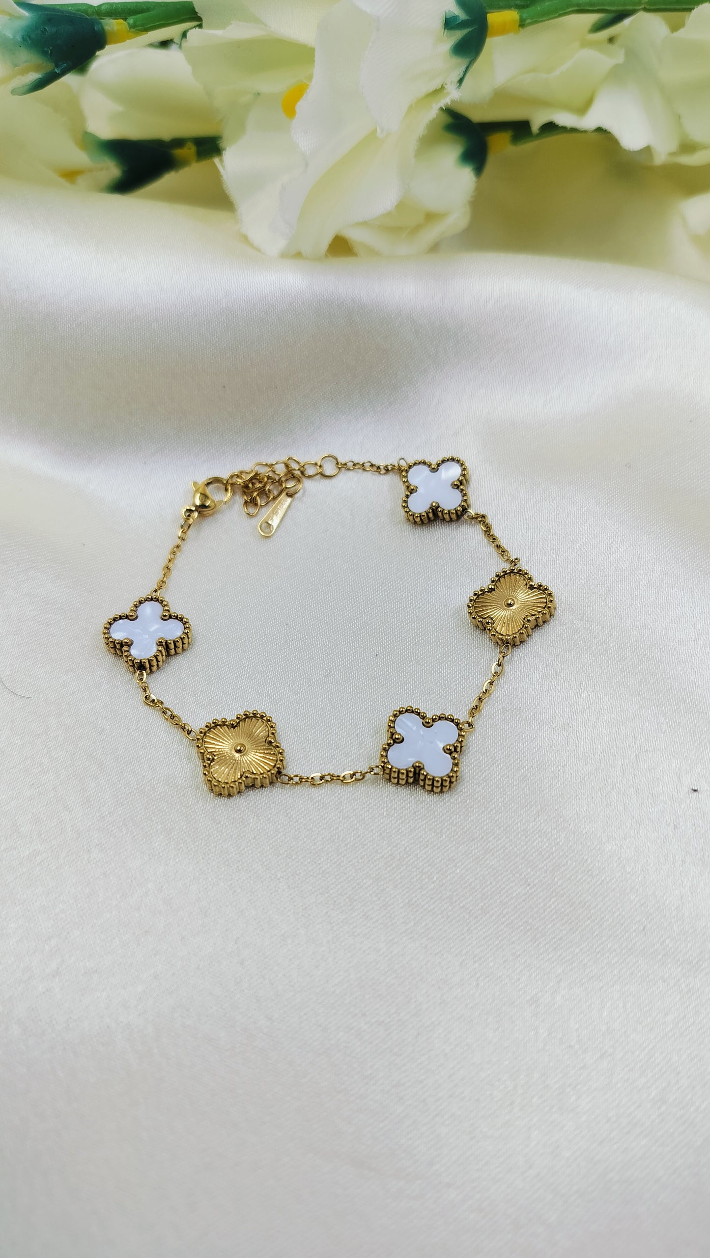 Gold bracelet with alternating white clover and floral charms, displayed on satin fabric – elegant luxury jewelry for women