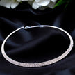 A silver choker necklace with a double line of sparkling stones, displayed against a black fabric background with white flowers.