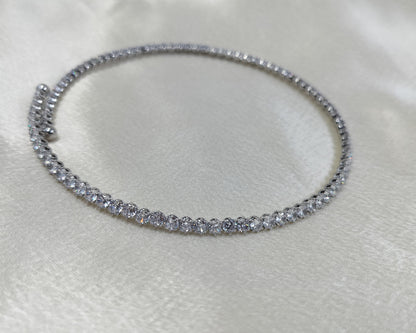 A close-up image of a silver choker necklace encrusted with cubic zirconia crystals, displayed on a white satin surface.