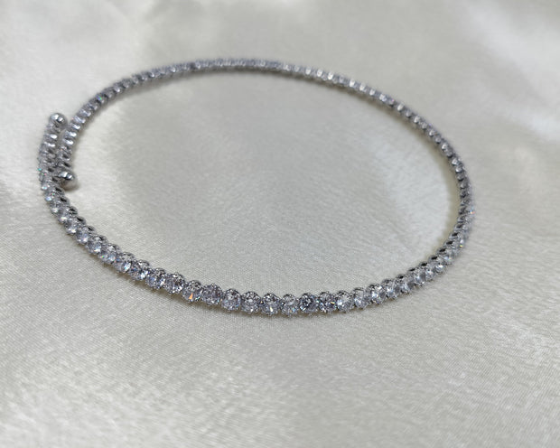 A close-up image of a silver choker necklace encrusted with cubic zirconia crystals, displayed on a white satin surface.