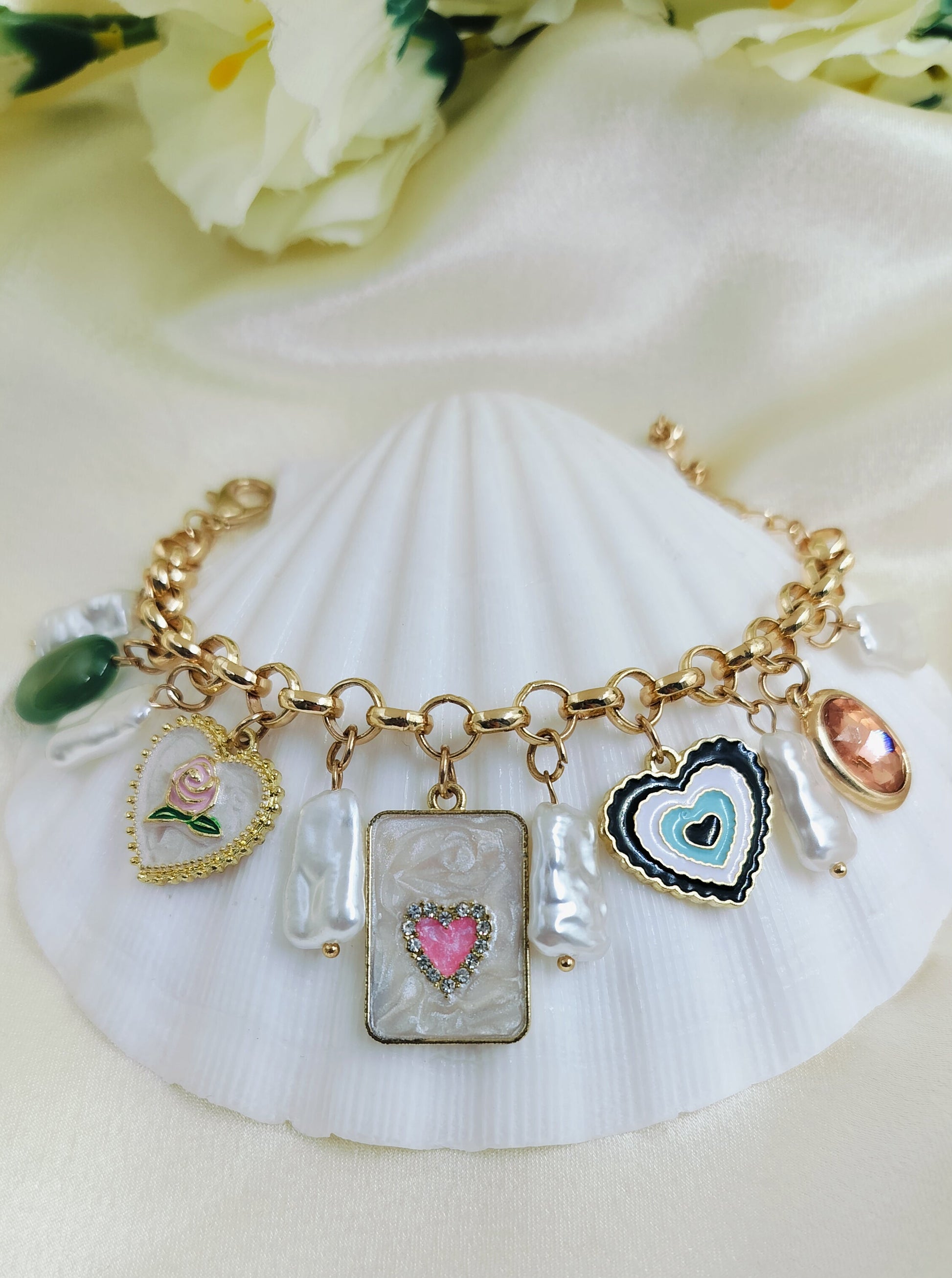 A gold-colored bracelet with various charms including a heart and floral design, displayed on a white surface.