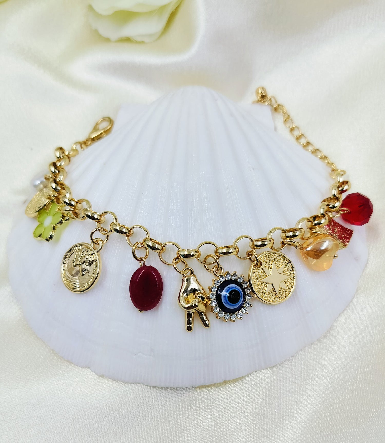 A gold-colored charm bracelet with various charms including an evil eye, Hamsa hand, star medallion, ancient coin, and floral accents displayed on a white surface.