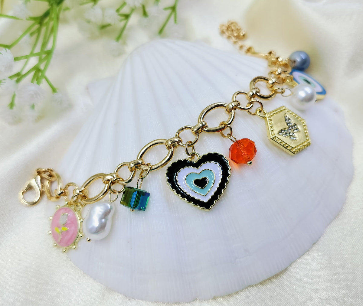 A gold charms bracelet with various pendants including an evil eye, hamsa hand, star medallion, and an ancient coin, displayed on a white surface.