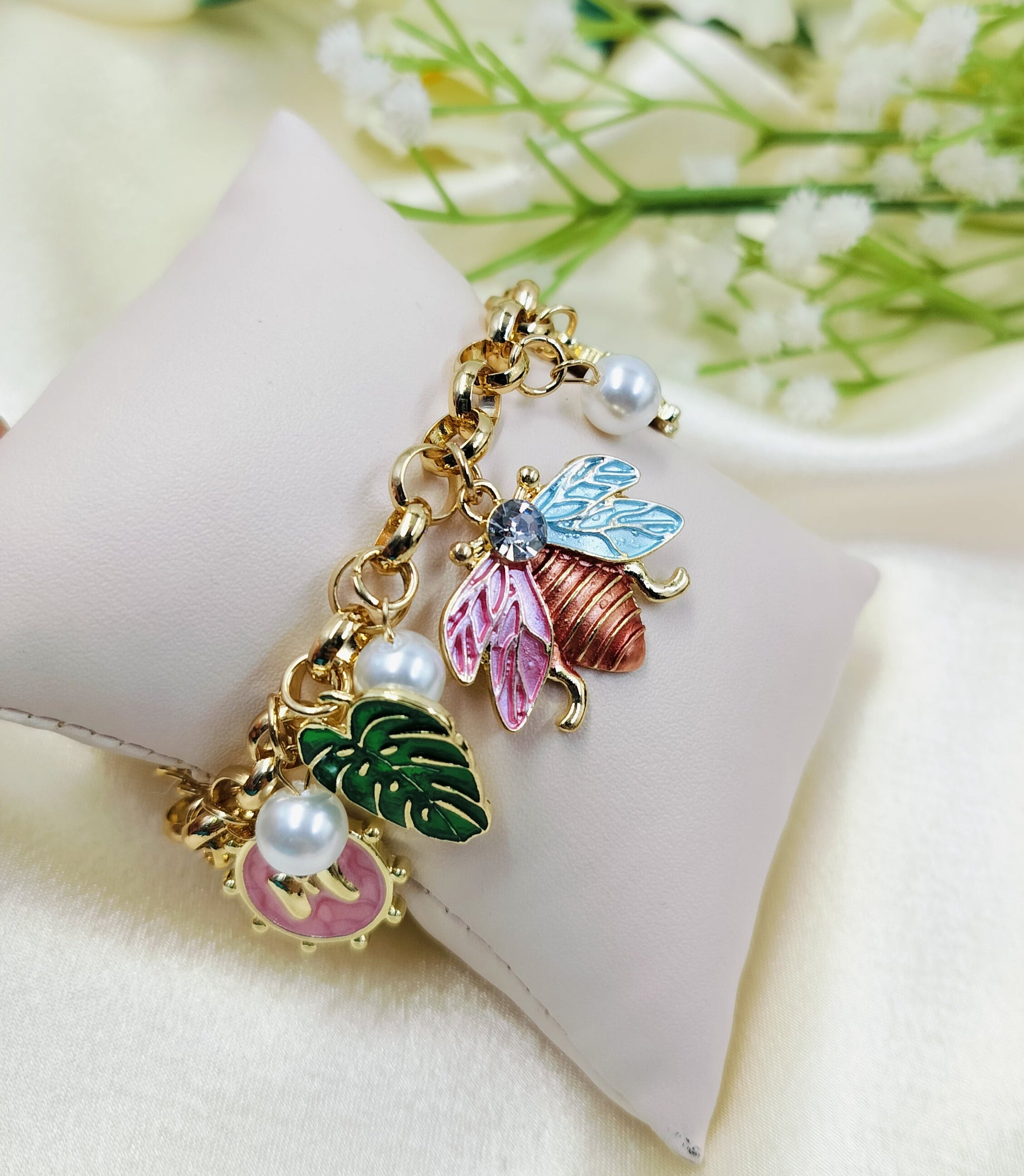 Gold charm bracelet with colorful butterfly, leaf, and pearl charms, elegant women's jewelry on cushion display